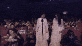 a woman in a white dress stands in front of a crowd of people with the words nineentertainment awards written on the bottom