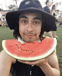 a man wearing a hat that says nyc club holds a slice of watermelon in front of his face