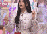 a woman in a white jacket and striped dress is standing in front of a microphone and holding something in her hand .