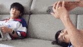two men are laying on a couch and one is taking a picture of the other with his phone .