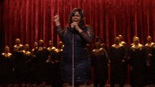 a woman singing into a microphone in front of a large choir