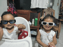 a baby wearing sunglasses sits next to a little girl