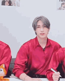 a man in a red shirt is sitting at a table with a pen in his hand and a stuffed animal .