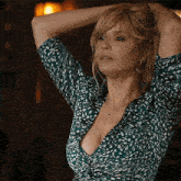 a woman in a green dress with a plunging neckline has her hands behind her head