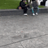 a man and a woman sit on a ledge looking at their cell phones