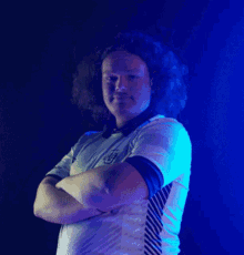 a man with curly hair is standing with his arms crossed and wearing a shirt with the letter u on it