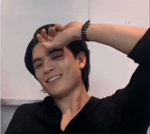 a man in a black shirt is smiling and covering his face with his hand .