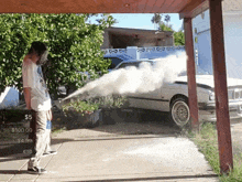 a man wearing a mask sprays a white car with a sign that says $ 5 $ 100.00 $ 4.99