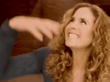 a woman with curly hair is laughing and pointing at something