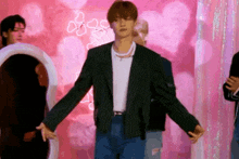 a man in a striped jacket is standing in front of a pink wall with hearts on it .