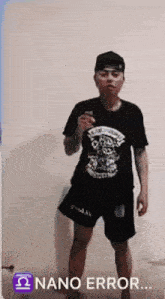 a man wearing a black shirt and black shorts is standing in front of a white wall holding a cell phone .