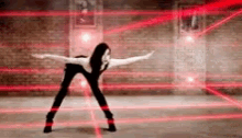 a woman is dancing in front of a brick wall with red lights behind her .