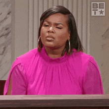 a woman in a pink dress is sitting at a judge 's table making a funny face .