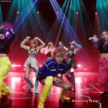 a group of women are dancing on a stage and the words hourlytsuki are on the bottom right