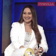 a woman in a white jacket is smiling in front of a pinkvilla banner