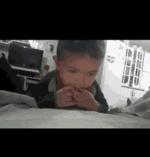 a young boy is laying on a bed with his hands on his mouth