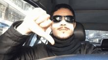 a man wearing sunglasses and a scarf is giving a thumbs down sign