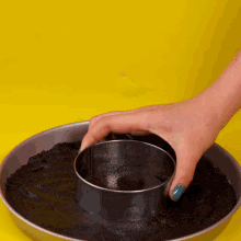 a person with blue nail polish is holding a metal ring over a pan of black crumbs