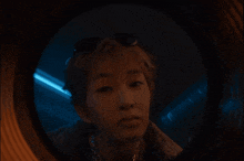 a person looking through a round window with a blue light in the background