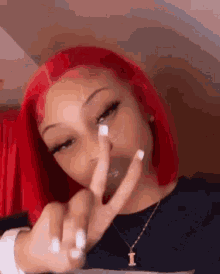 a woman with red hair and white nails is making a peace sign with her fingers .
