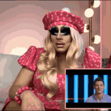 a drag queen wearing a pink dress and a red hat talks to a man