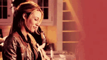 a woman in a leather jacket is standing in a kitchen holding a glass of wine .