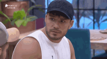 a man with a beard wearing a white tank top and a black hat