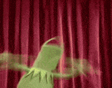 kermit the frog is dancing on a stage with a red curtain behind him .