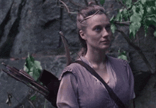 a woman in a purple dress is holding an arrow and bow .