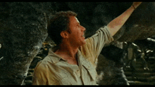 a man in a tan shirt is reaching up towards something