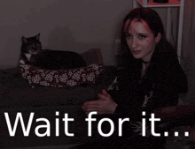 a woman sitting on a couch with a cat in a cat bed and the words wait for it