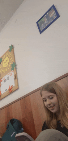 a girl is reading a book in front of a bulletin board with a sun on it that says acacia