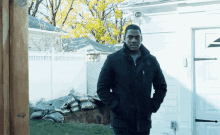 a man in a black coat stands in front of a house