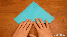 a person folding a piece of blue paper on a wooden table