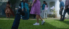 a woman in a purple dress is walking in a crowd of people with xtoms120505 on the bottom