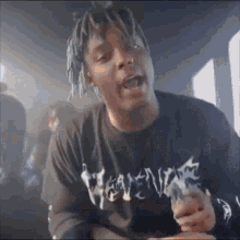 a man with dreadlocks is smoking a cigarette and wearing a black t-shirt with the word heaven on it .