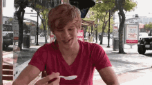 a young man in a red t-shirt is eating ice cream with a spoon .
