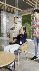 a man with a lanyard around his neck is sitting in a chair while another man stands behind him