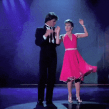 a man in a tuxedo stands next to a woman in a pink dress on a stage