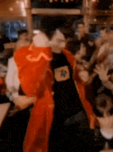 a man in a red jacket and black shirt is dancing in a crowd of people .
