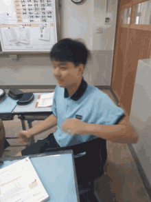 a boy in a blue shirt is sitting at a desk in front of a white board with chinese characters on it