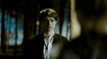 a man in a black jacket and white shirt is standing in a dark room looking at another man .