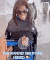 a woman wearing sunglasses and a black sweater is standing in front of a sign that says she wanted her story heard