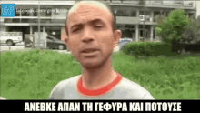 a man in a gray shirt with a red collar stands in front of a grassy field with a facebook logo in the corner