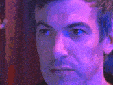 a close up of a man 's face with a purple light behind him