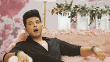 a man in a black shirt is sitting on a pink couch with his mouth open