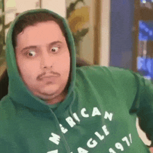 a man wearing a green hoodie with the word american eagle on it is making a funny face .