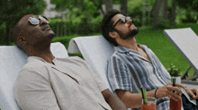 a man wearing sunglasses sits next to another man in a lounge chair