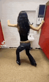 a woman is dancing in a bathroom in front of a red wall .