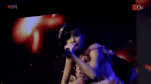 two women singing into microphones on a stage with the words live on the bottom